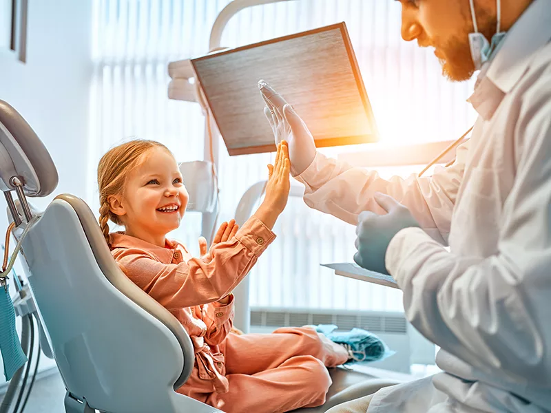Program dla stomatologa - dziecko siedzące na fotelu dentystycznym, przybija piątkę ze stomatologiem